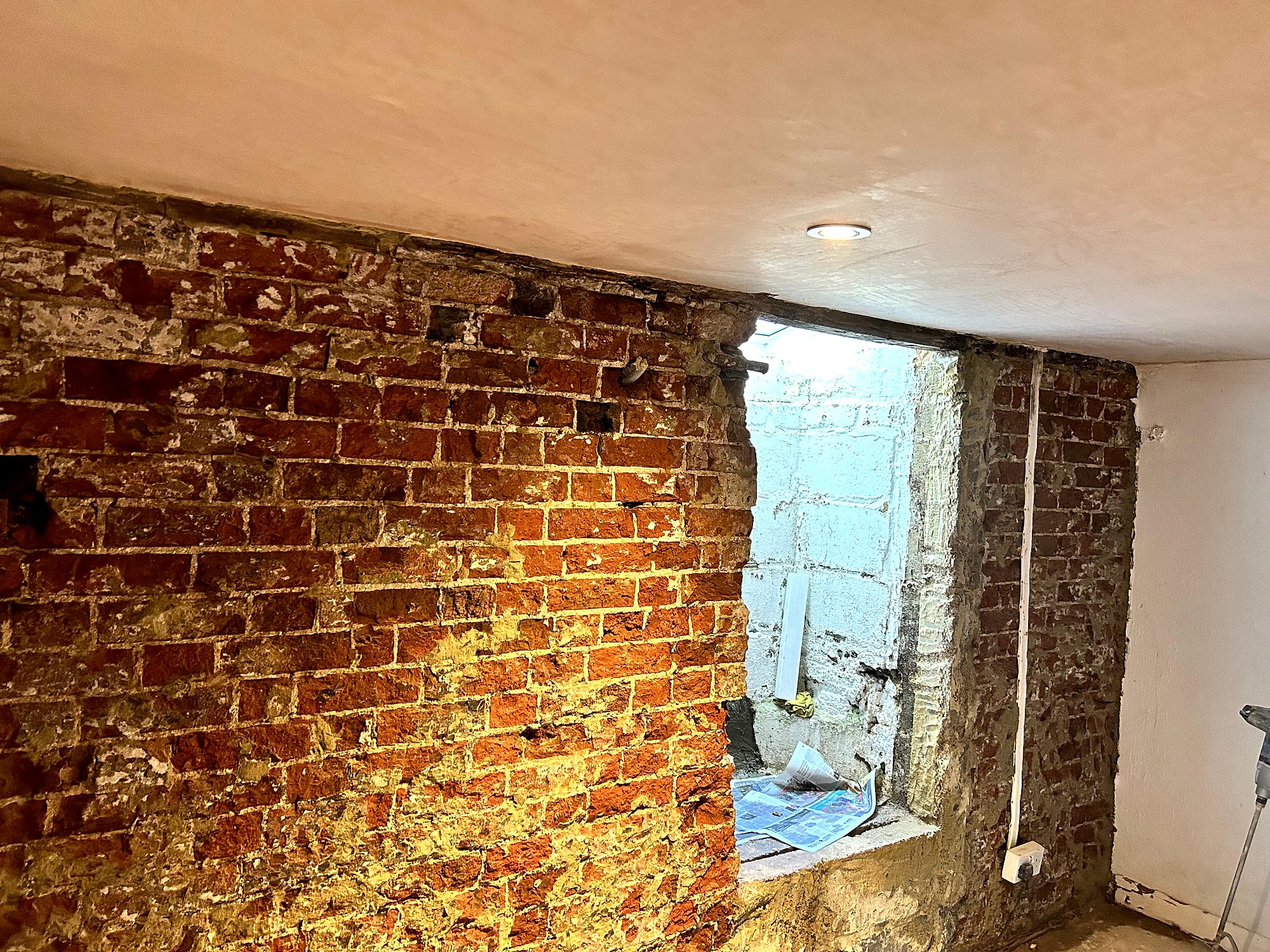 Basement with freshly skimmed ceiling above exposed period brick walls during renovation in East Kent