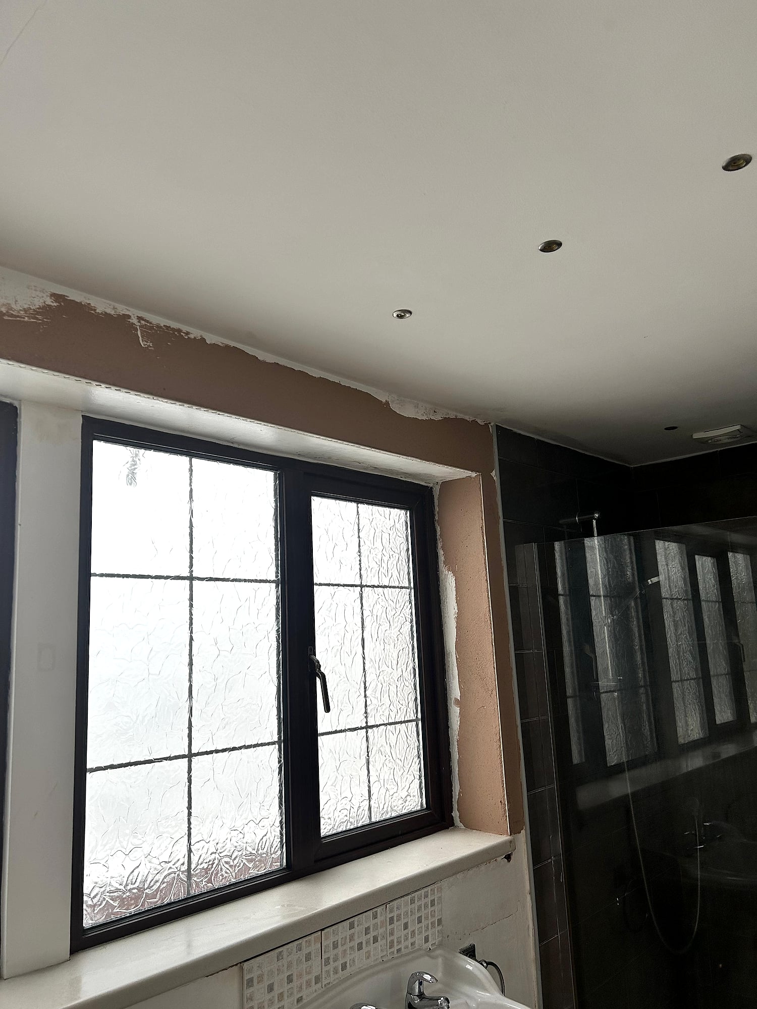 Bathroom window reveal freshly plastered with black frame window and shower enclosure in Kent home