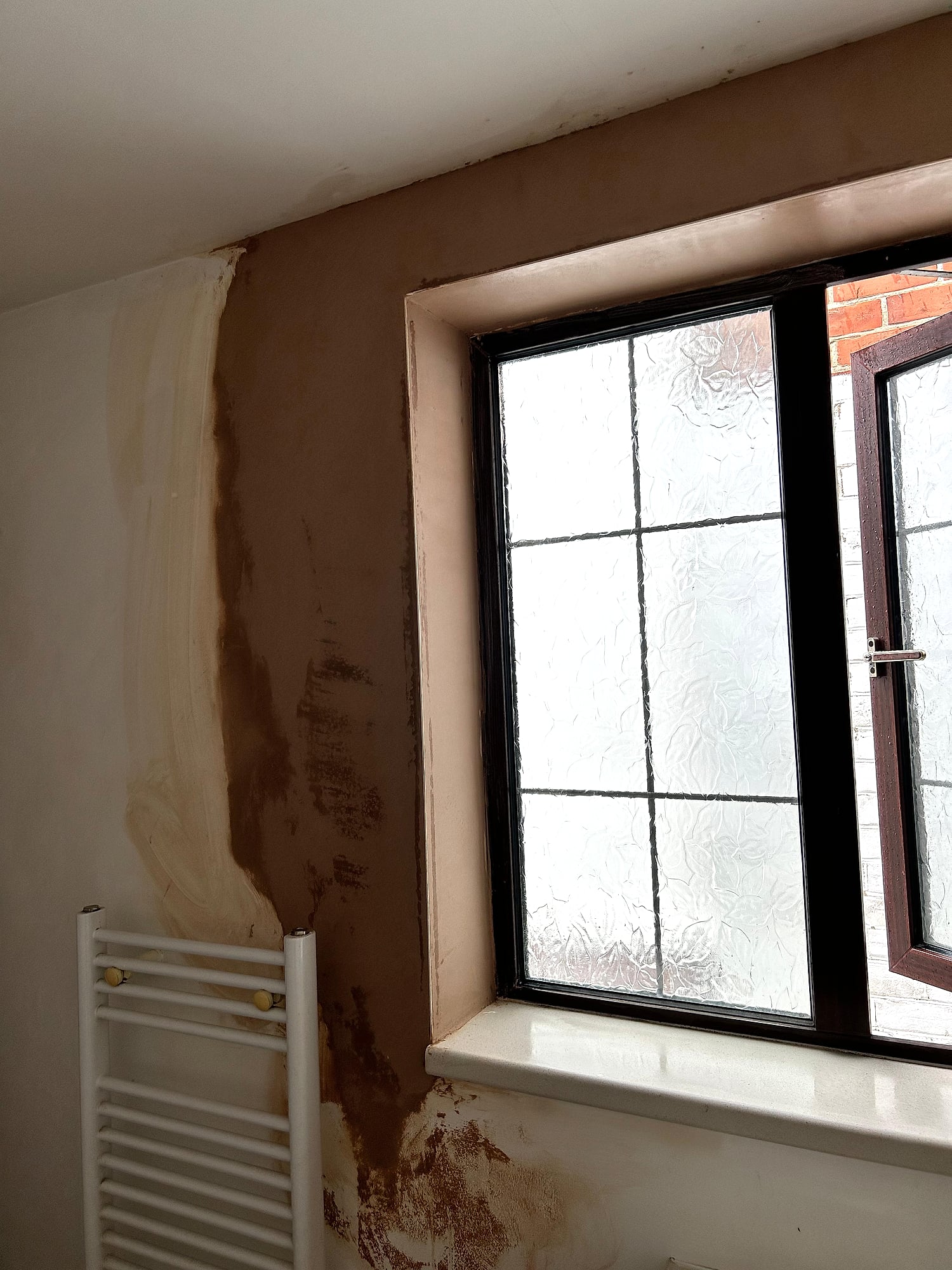 Bathroom window reveal freshly plastered with frosted leaded glass and towel radiator in Kent home