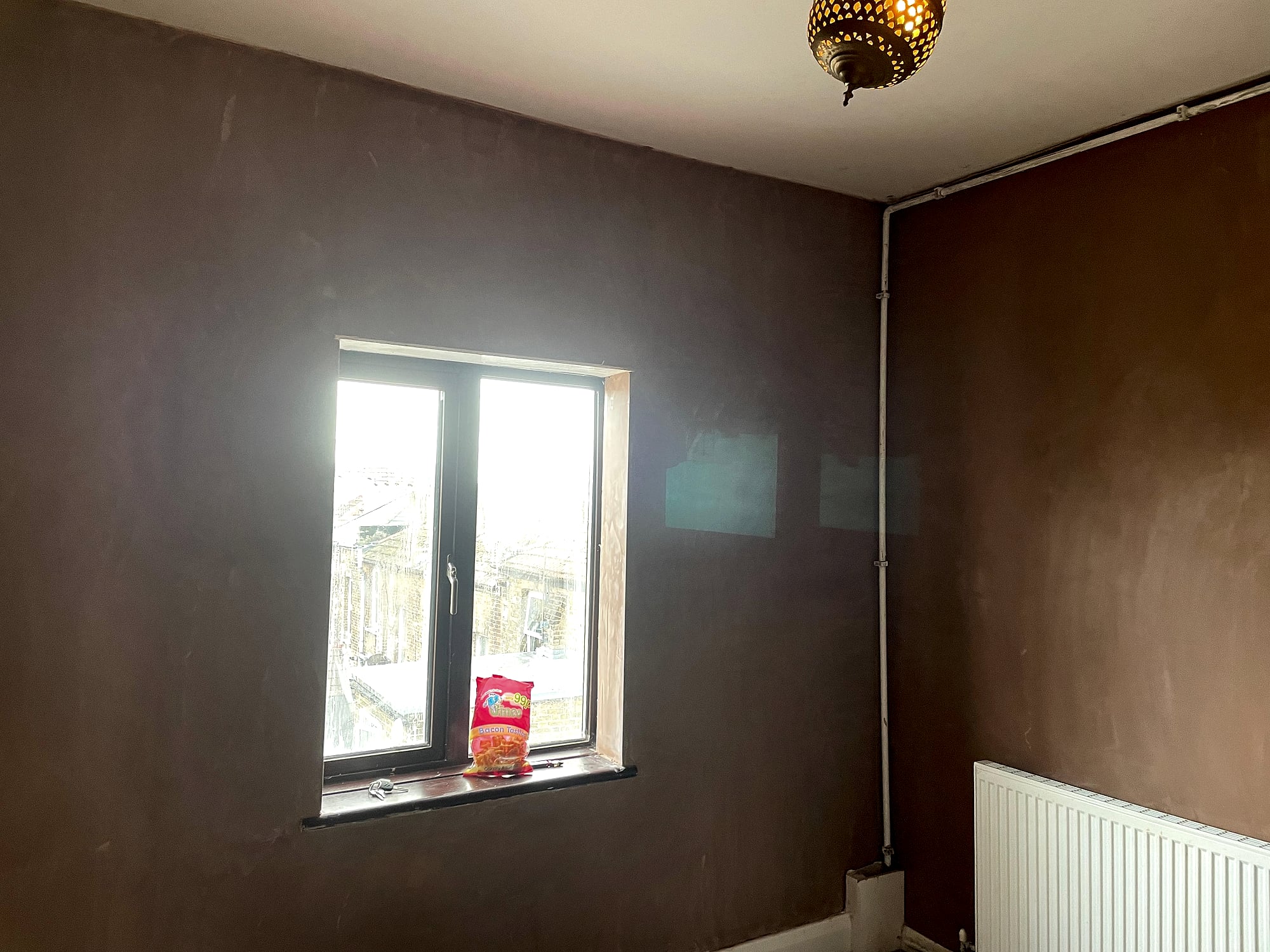 Bedroom with freshly plastered walls and window with Moroccan pendant light showing rooftop views in Kent