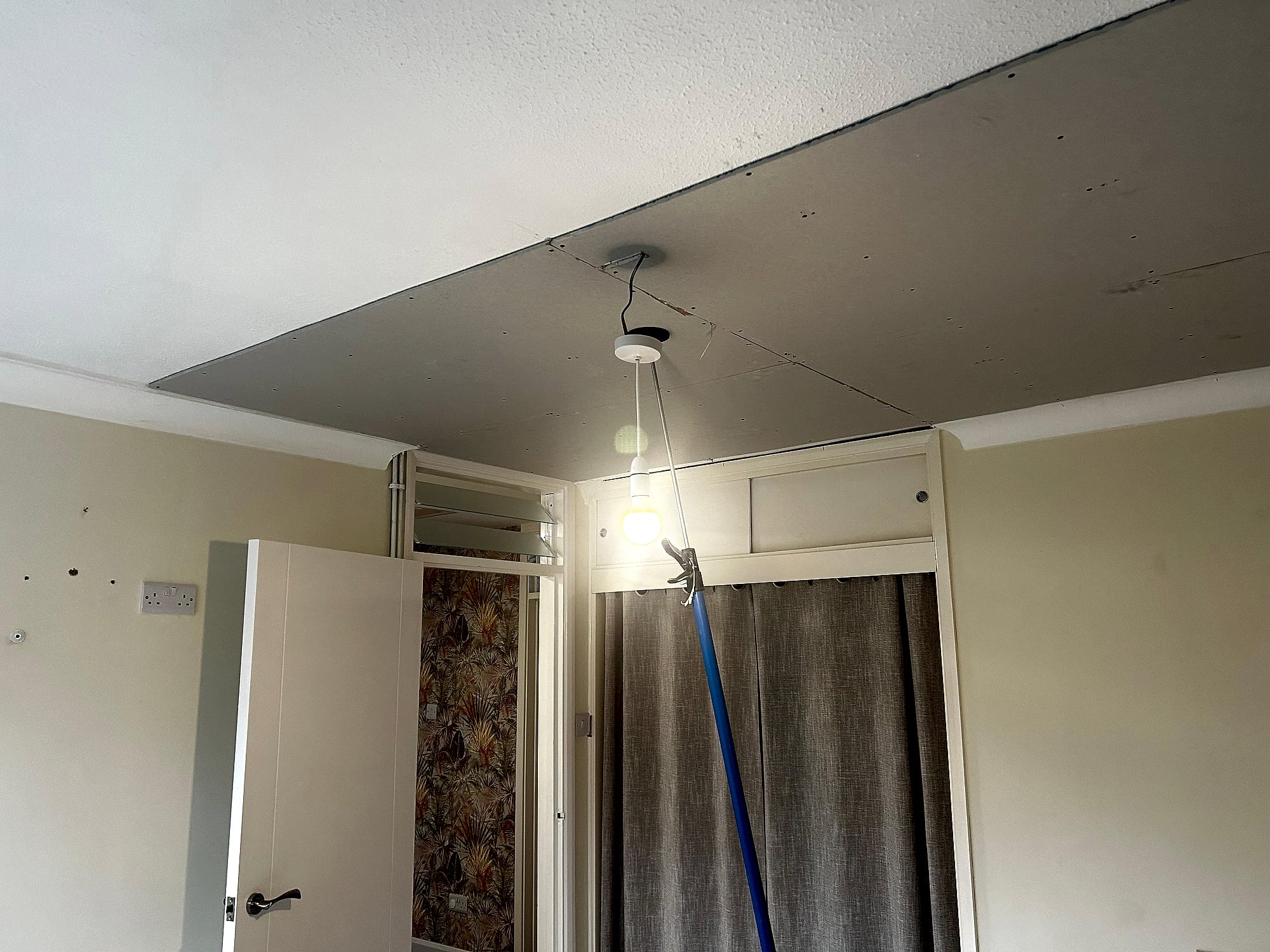Bedroom with lowered plasterboard ceiling from different angle showing doorway and wallpapered room beyond in Kent