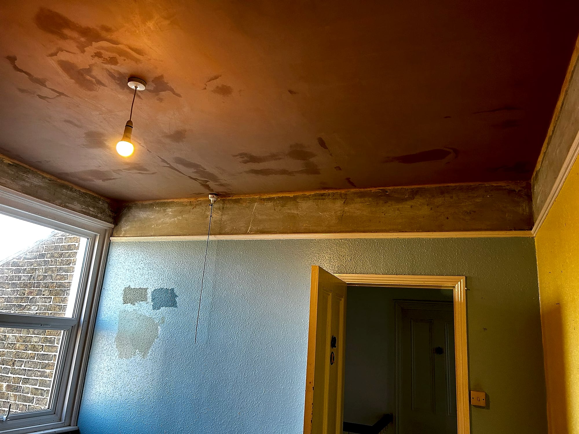 Room before plastering showing damaged peeling ceiling with plasterboard patches and stripped walls in Kent