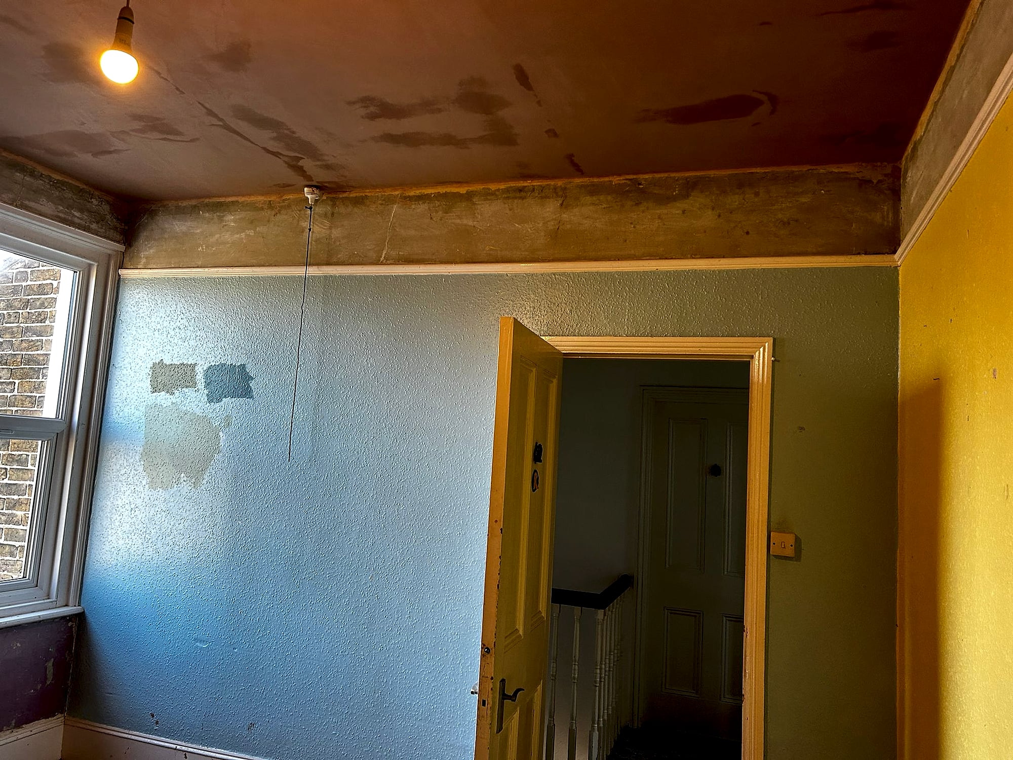Room before plastering showing badly damaged ceiling with peeling paint and stained walls in Kent property