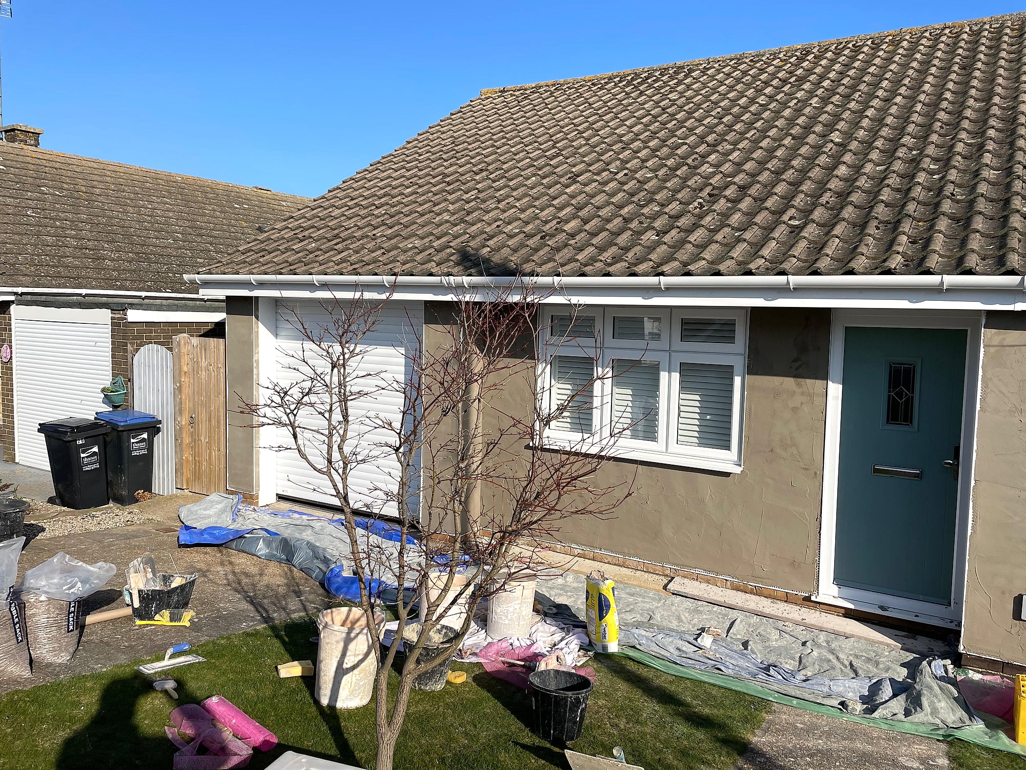 Bungalow exterior during rendering with dust sheets and materials on the ground in Kent