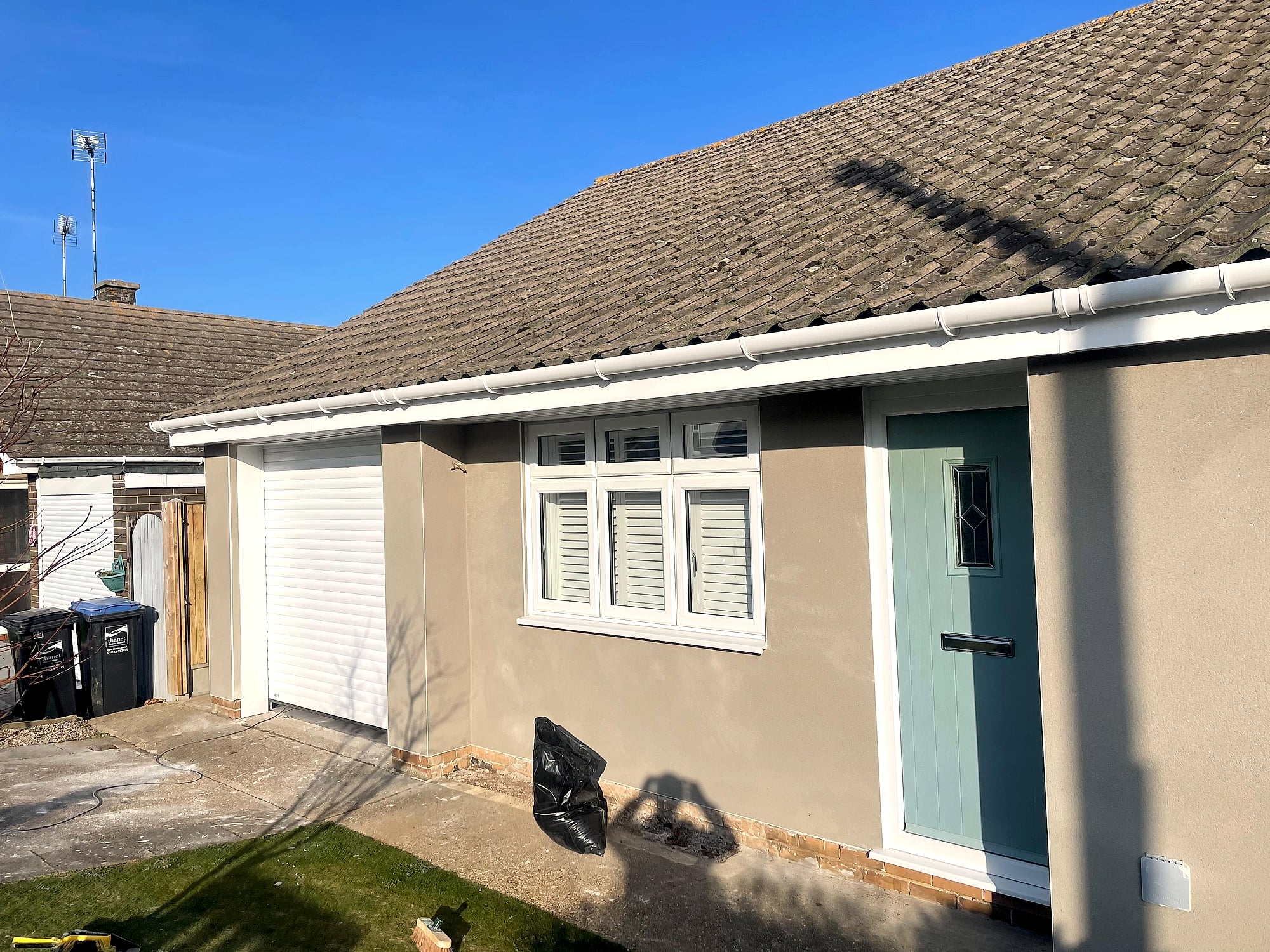 Completed bungalow with smooth rendered exterior walls and green front door viewed from garden in Kent