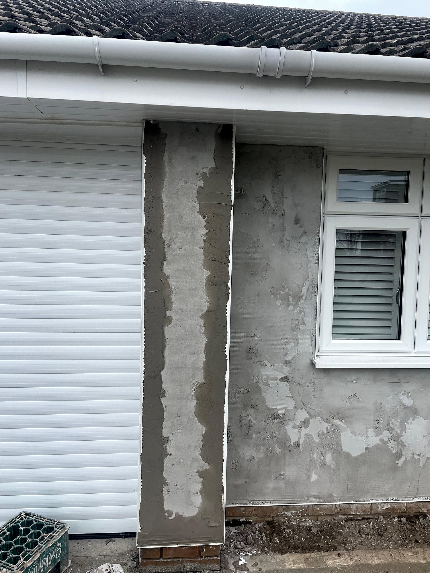 Bungalow exterior render being applied showing wet sand and cement next to garage roller door in Kent