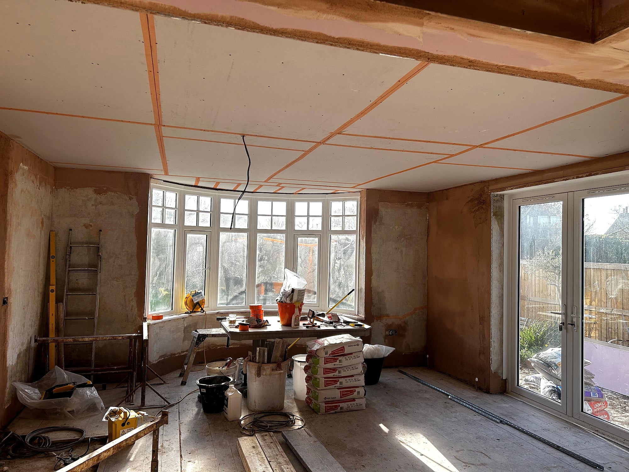 Plasterboard ceiling being fitted in living room with bay window and patio doors in Kent renovation