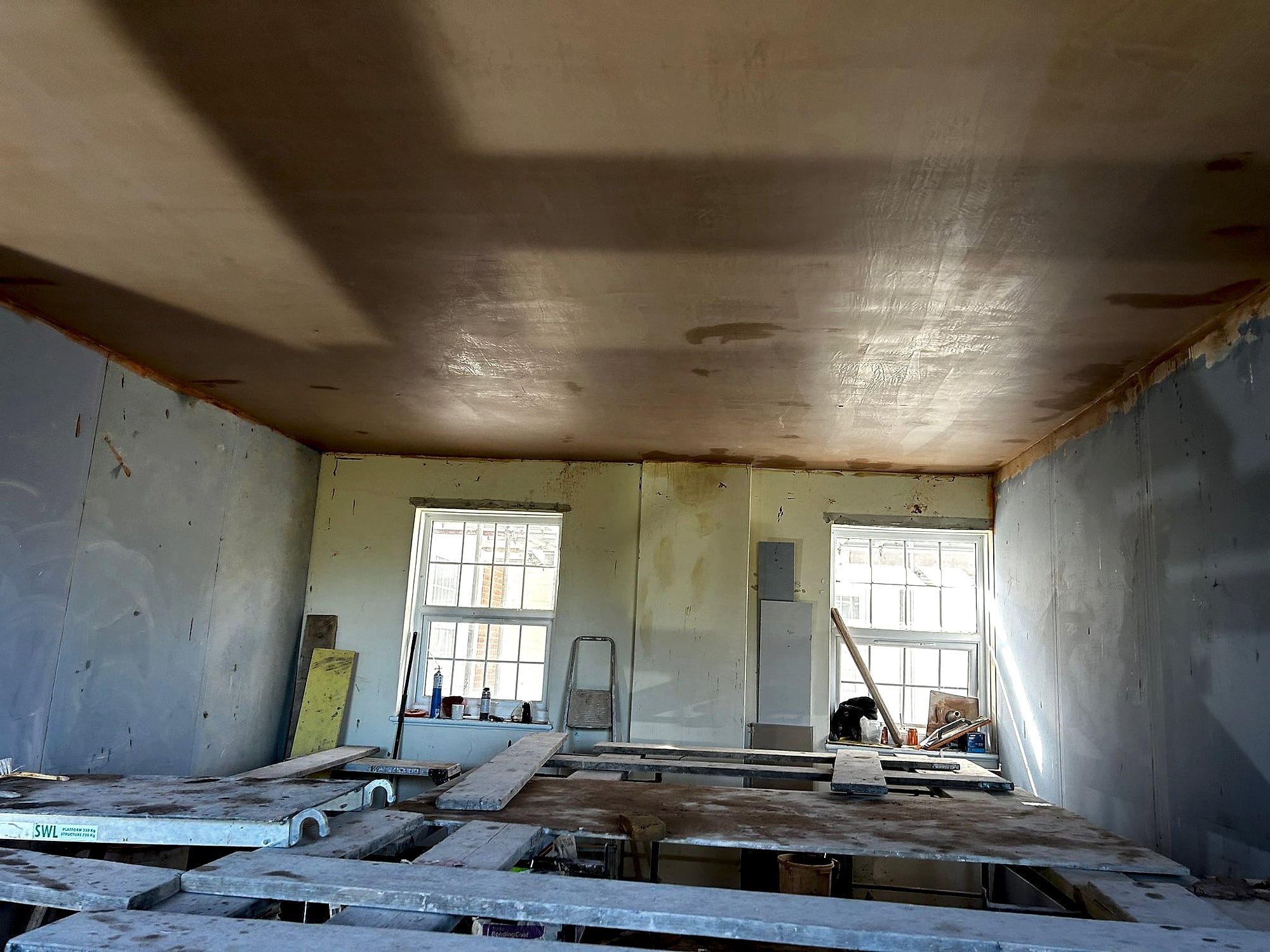 Large room ceiling freshly skimmed from scaffolding platform with dry lined walls below in Kent