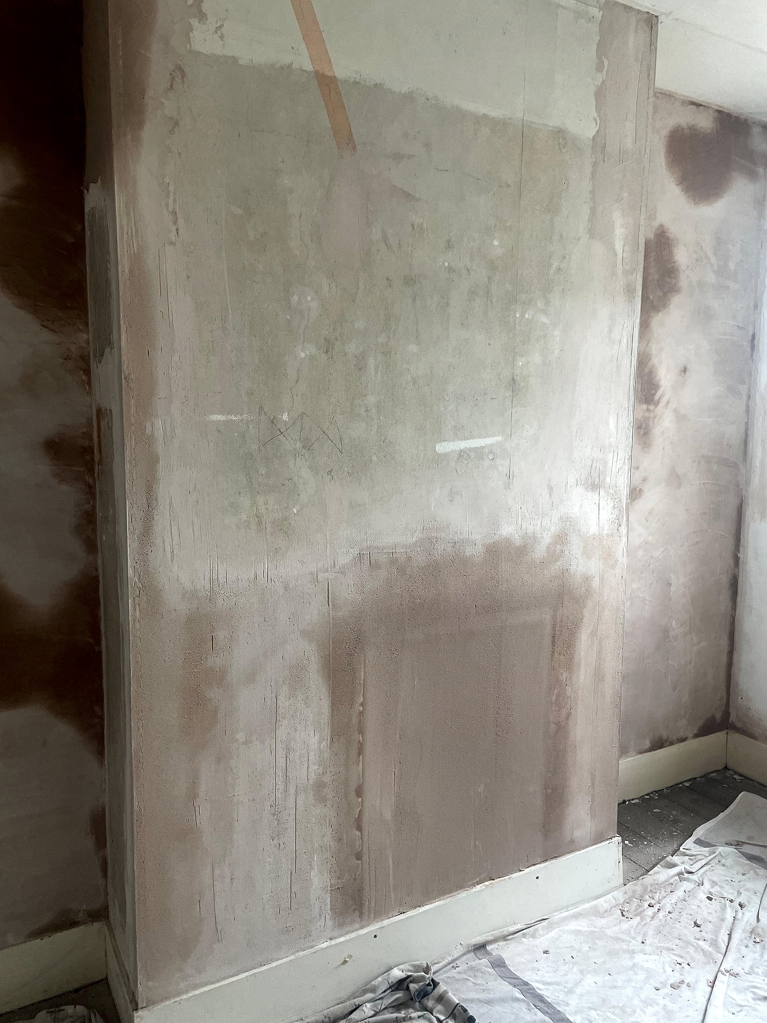 Chimney breast and walls during skim coat plastering with dust sheets covering furniture in Kent home