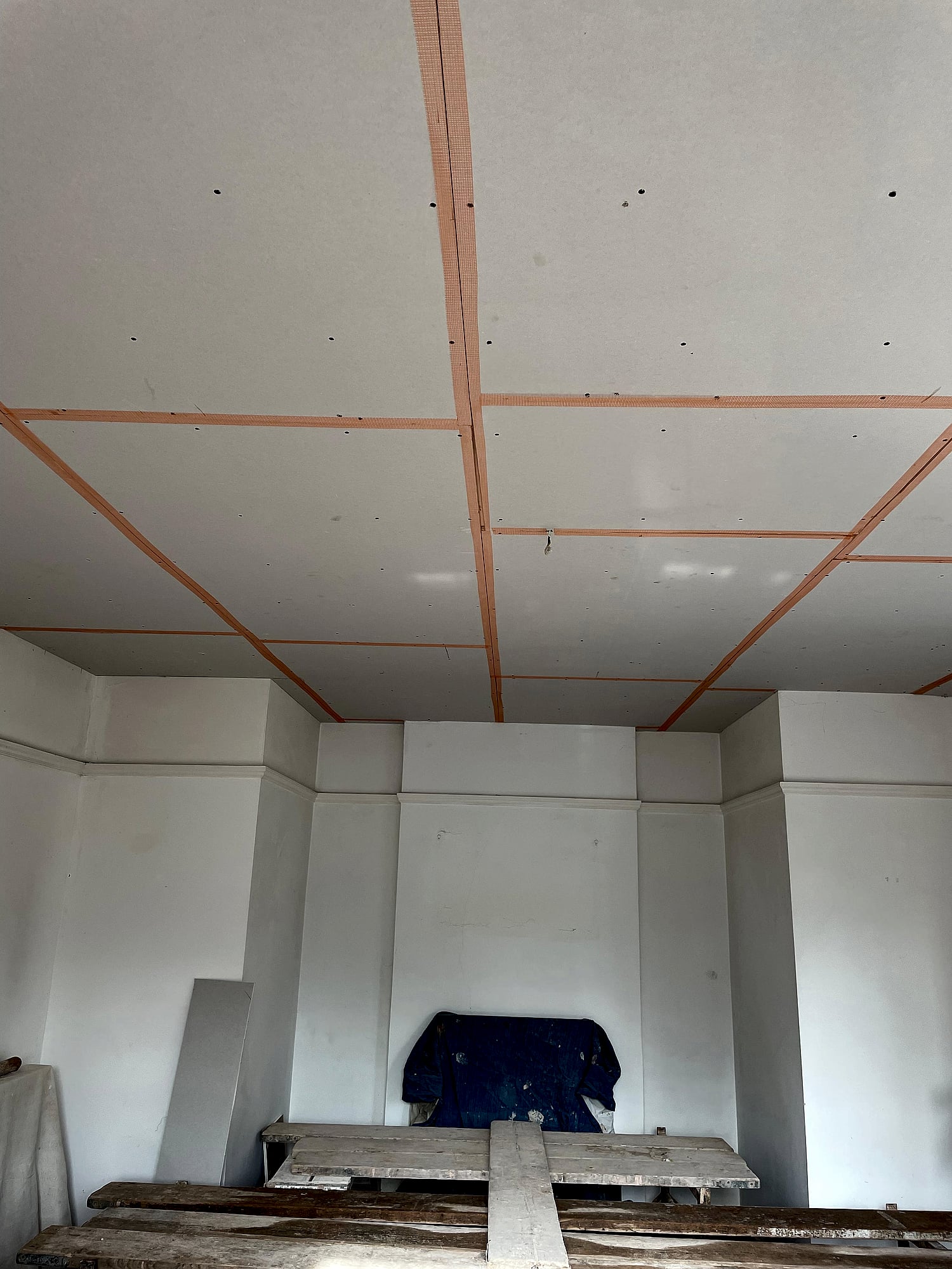 Plasterboard ceiling with scrim tape joints ready for skimming in large room with boarding and scaffolding in Kent