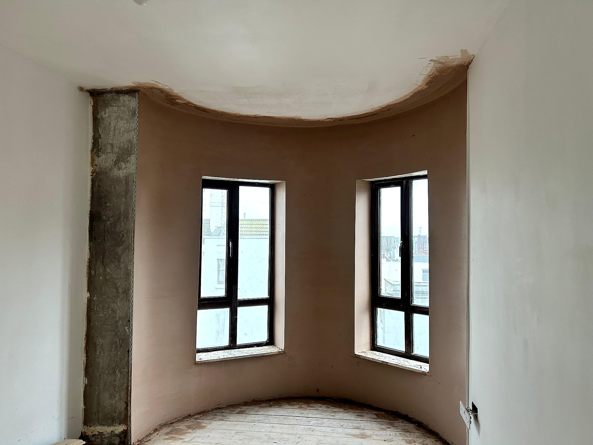 Wide view of curved bay window with fresh skim plaster and concrete column in period Kent property renovation