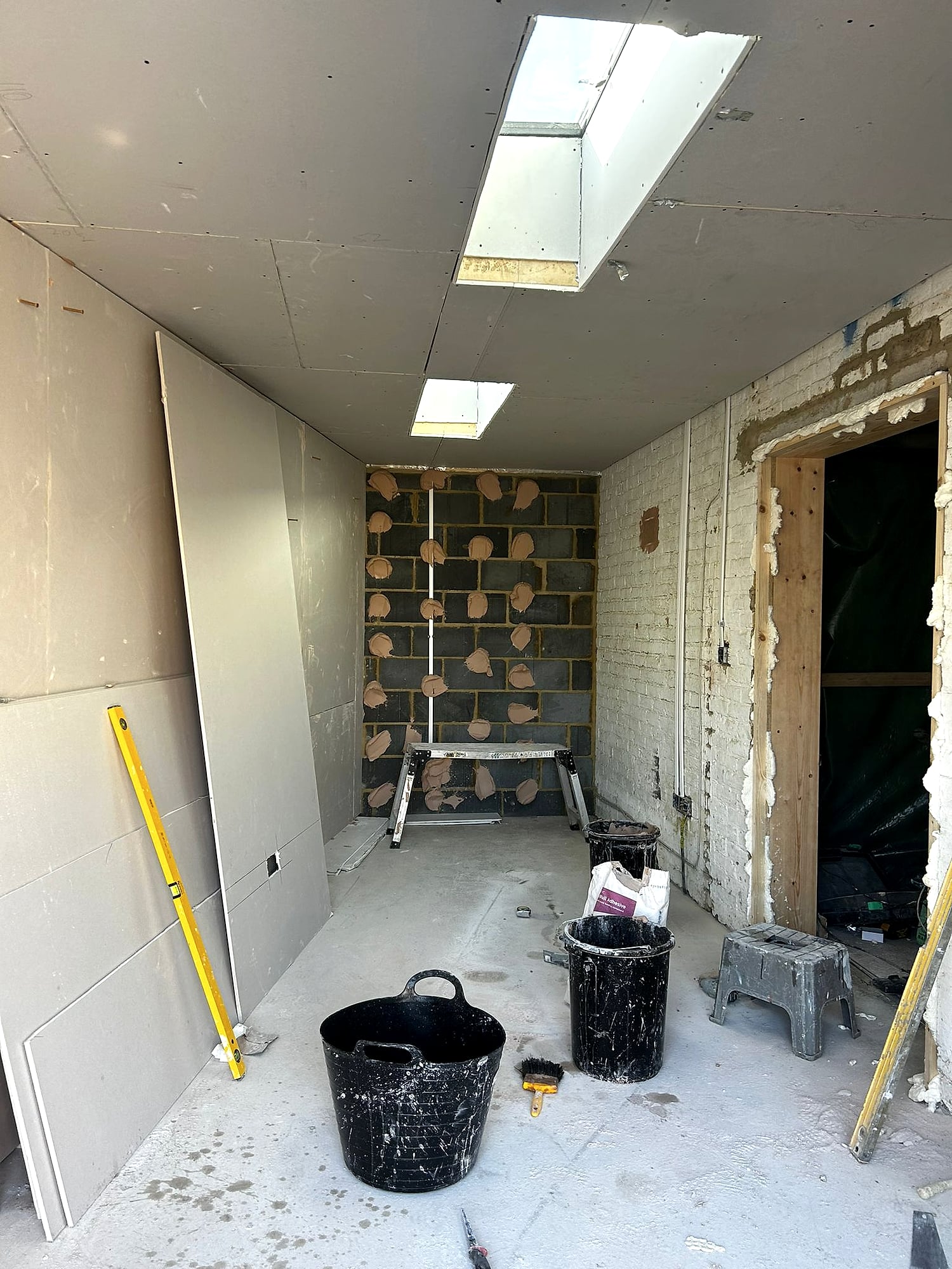 Extension with plasterboard walls and ceiling being fitted around skylights with adhesive dabs visible in Kent