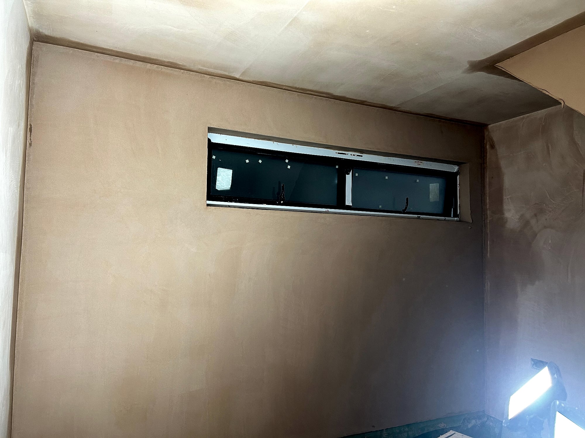 Extension wall freshly plastered with smooth skim coat around narrow horizontal window in Kent new build