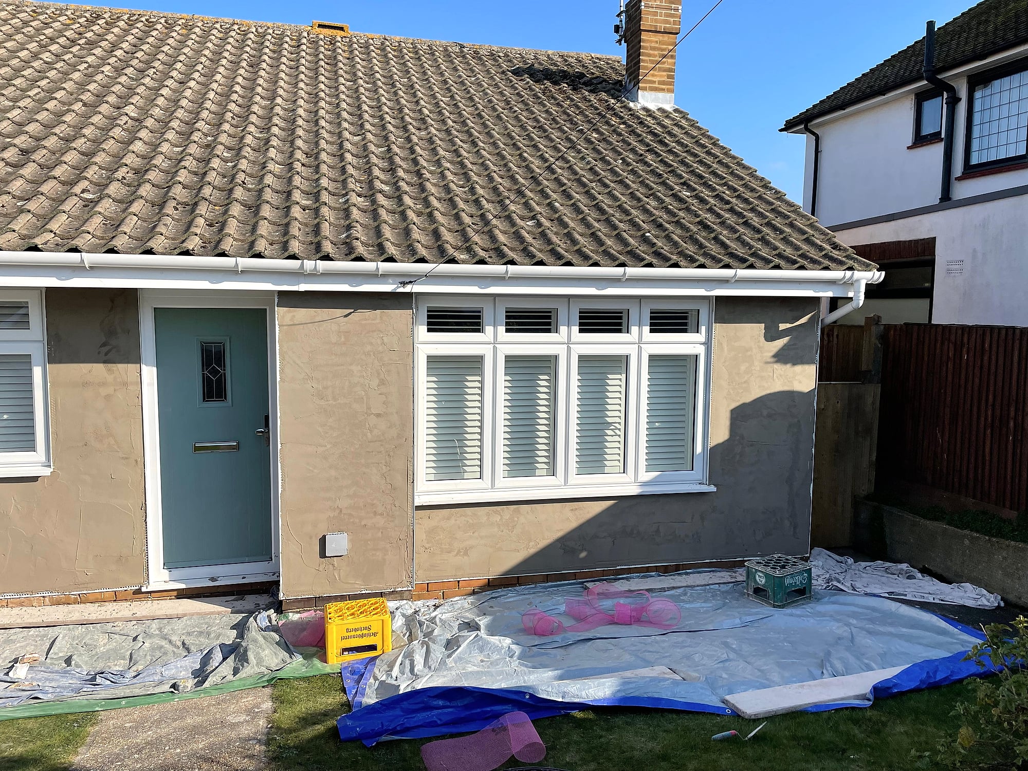 Freshly applied sand and cement render on house exterior wall with window viewed from scaffolding in Kent