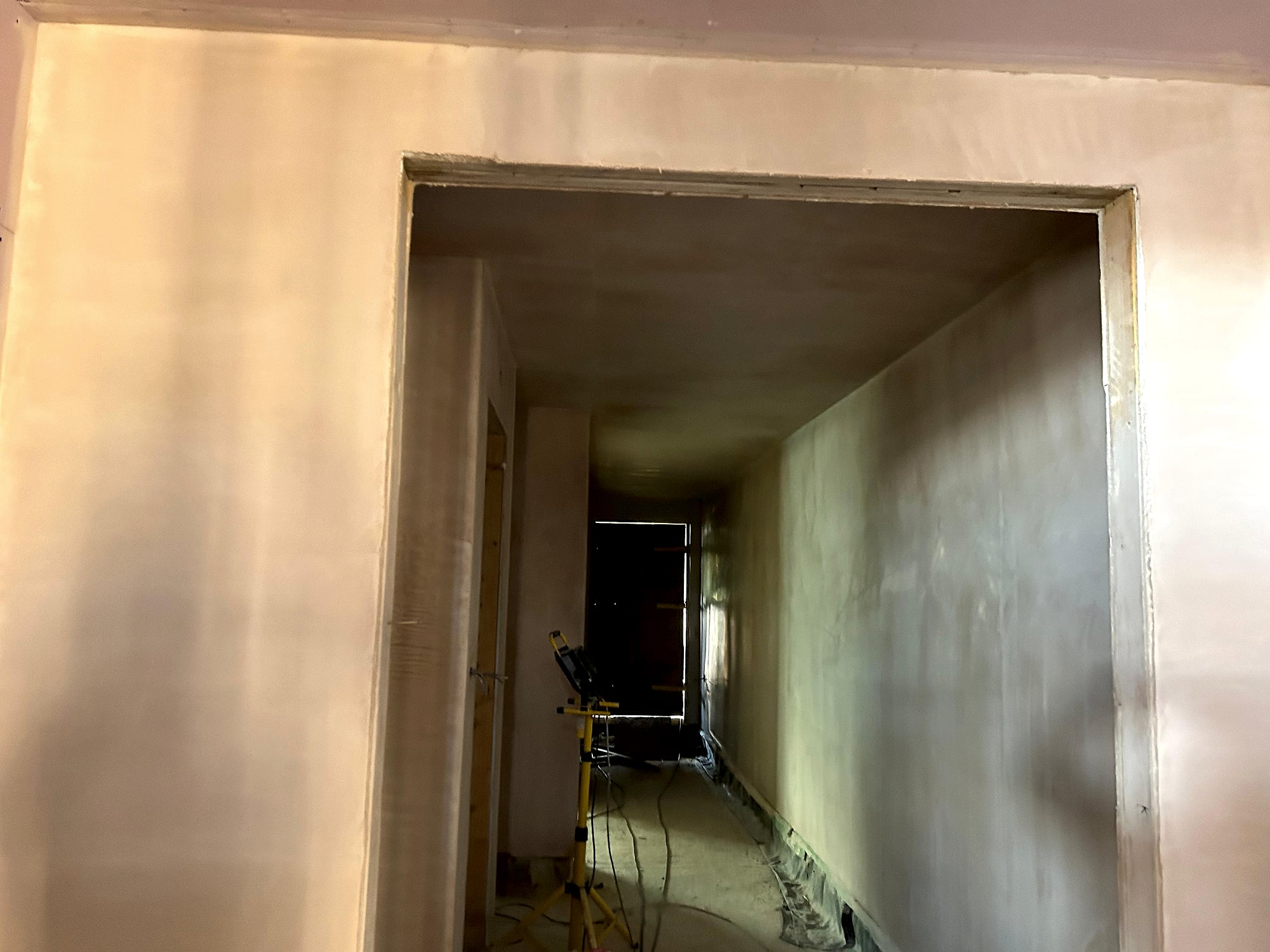 Hallway with freshly plastered door reveal and smooth skim coat on walls with work light in Kent renovation