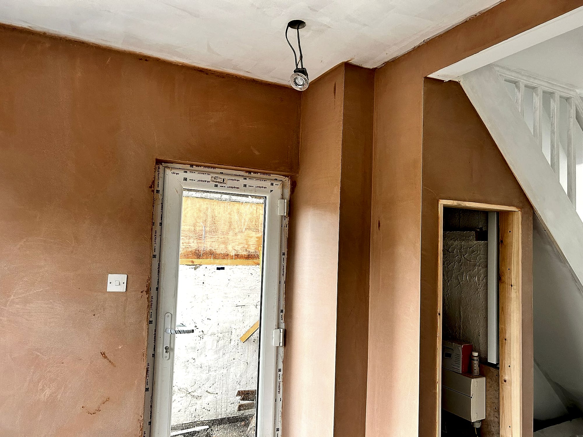 Hallway freshly plastered showing new door opening with staircase and under-stairs cupboard in Kent renovation