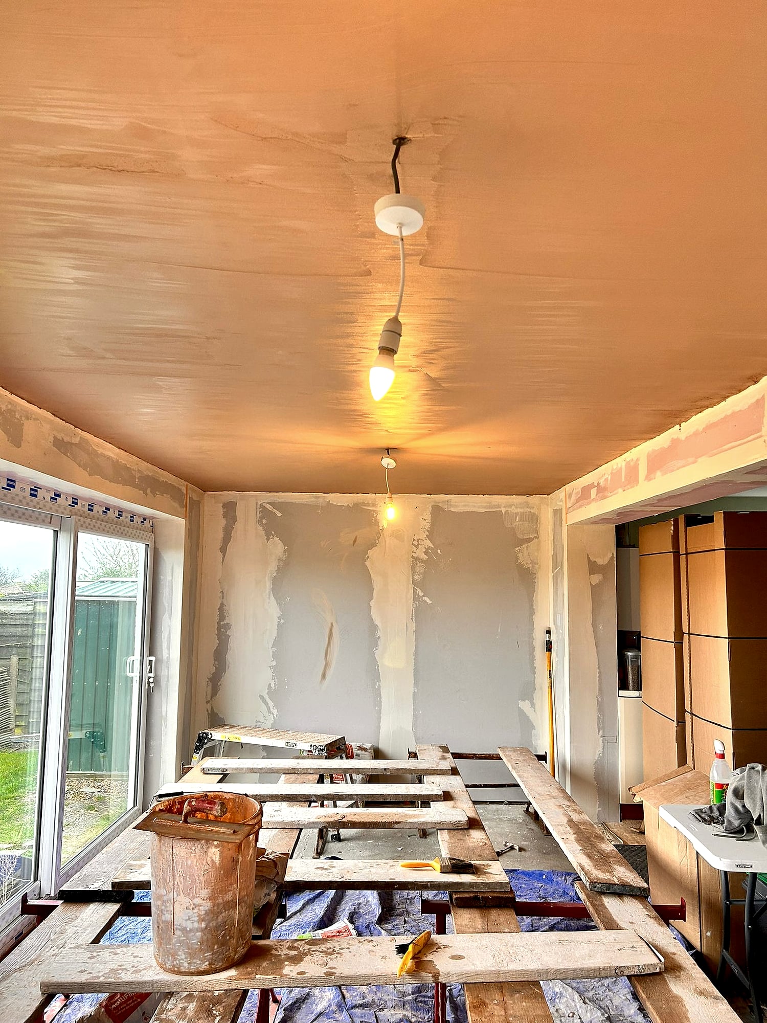 Kitchen ceiling being skimmed from scaffolding platform with plasterboard walls and patio door in Kent extension