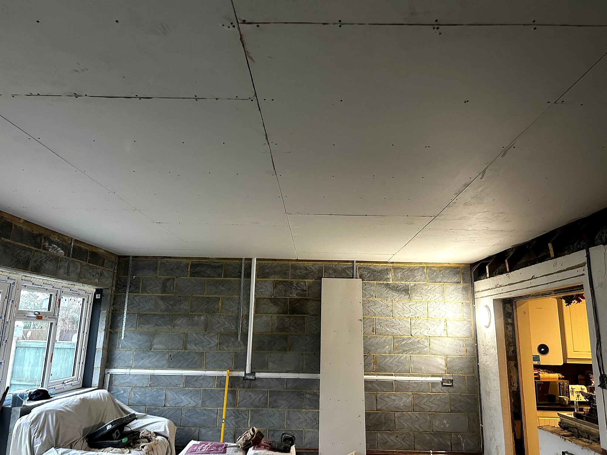 Plasterer fitting plasterboard ceiling in blockwork extension with boarding tools visible in Kent