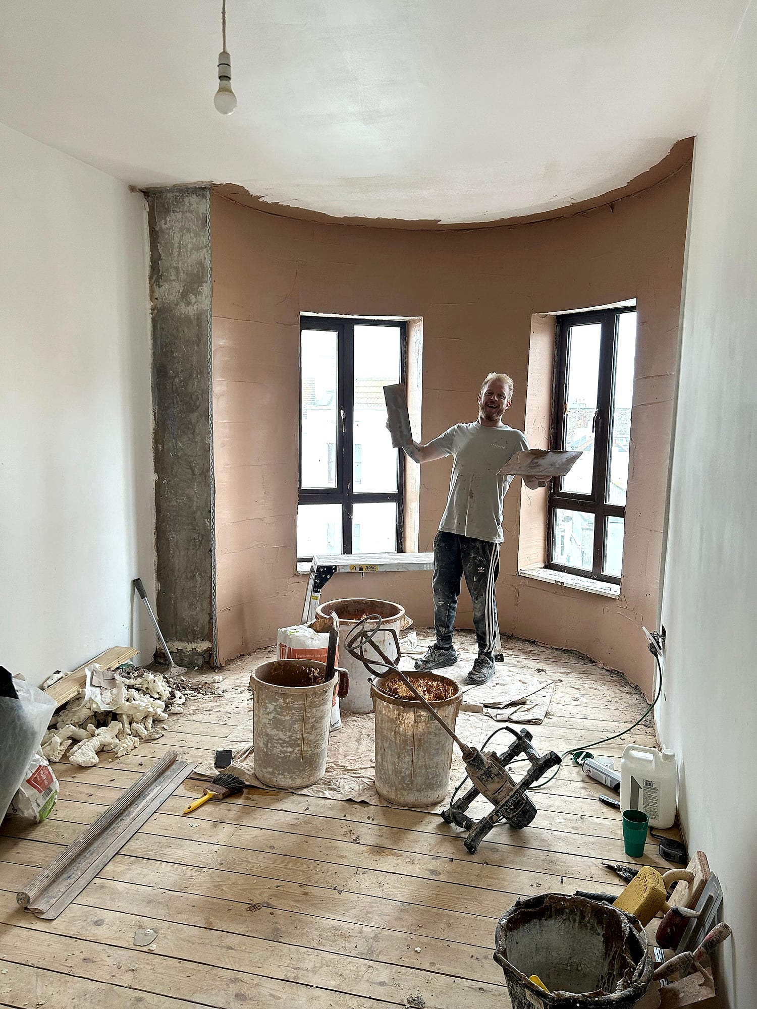 Lee Wehrle plastering a curved bay window holding hawk and trowel in period East Kent property renovation