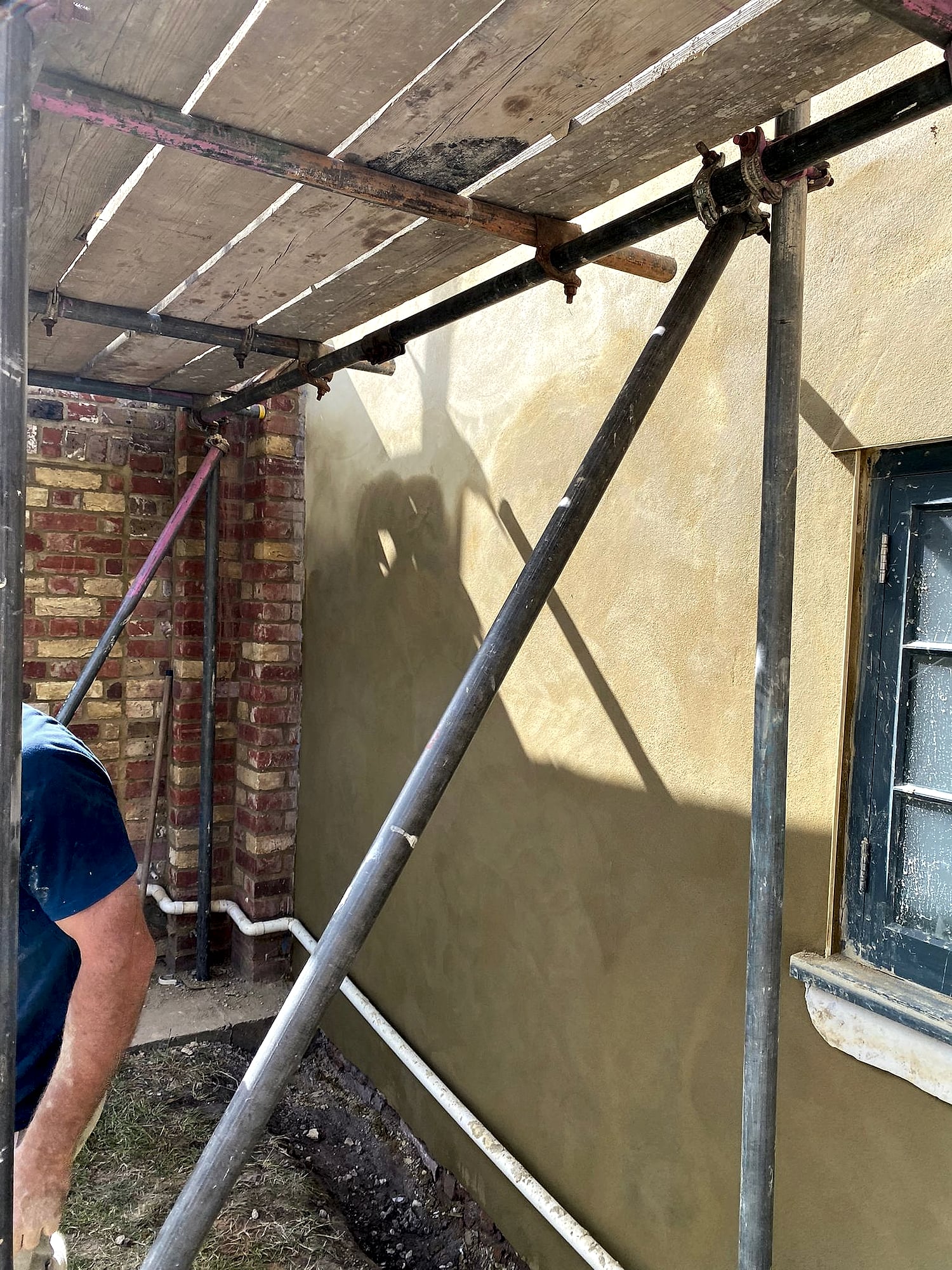 Plasterer working on scaffolding applying sand and cement render to period property exterior in East Kent