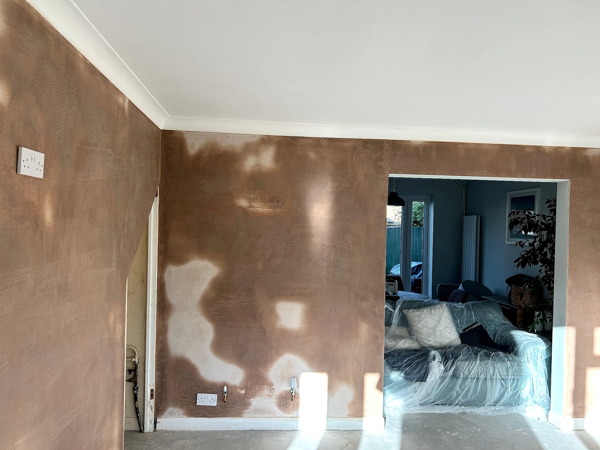 Freshly plastered living room walls with dust-sheeted furniture visible through doorway in Kent home