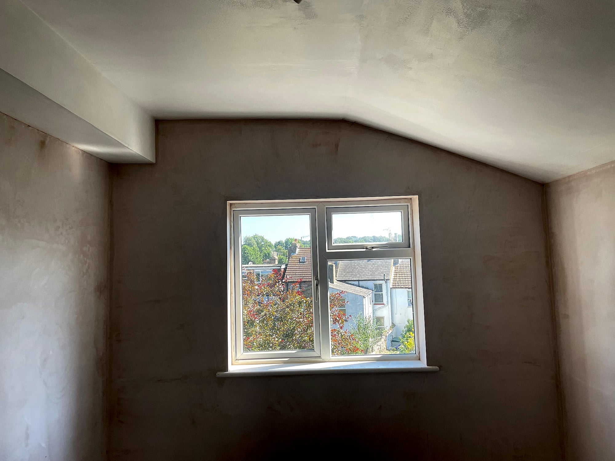 Loft conversion room with freshly skimmed walls following roofline and window overlooking Kent rooftops
