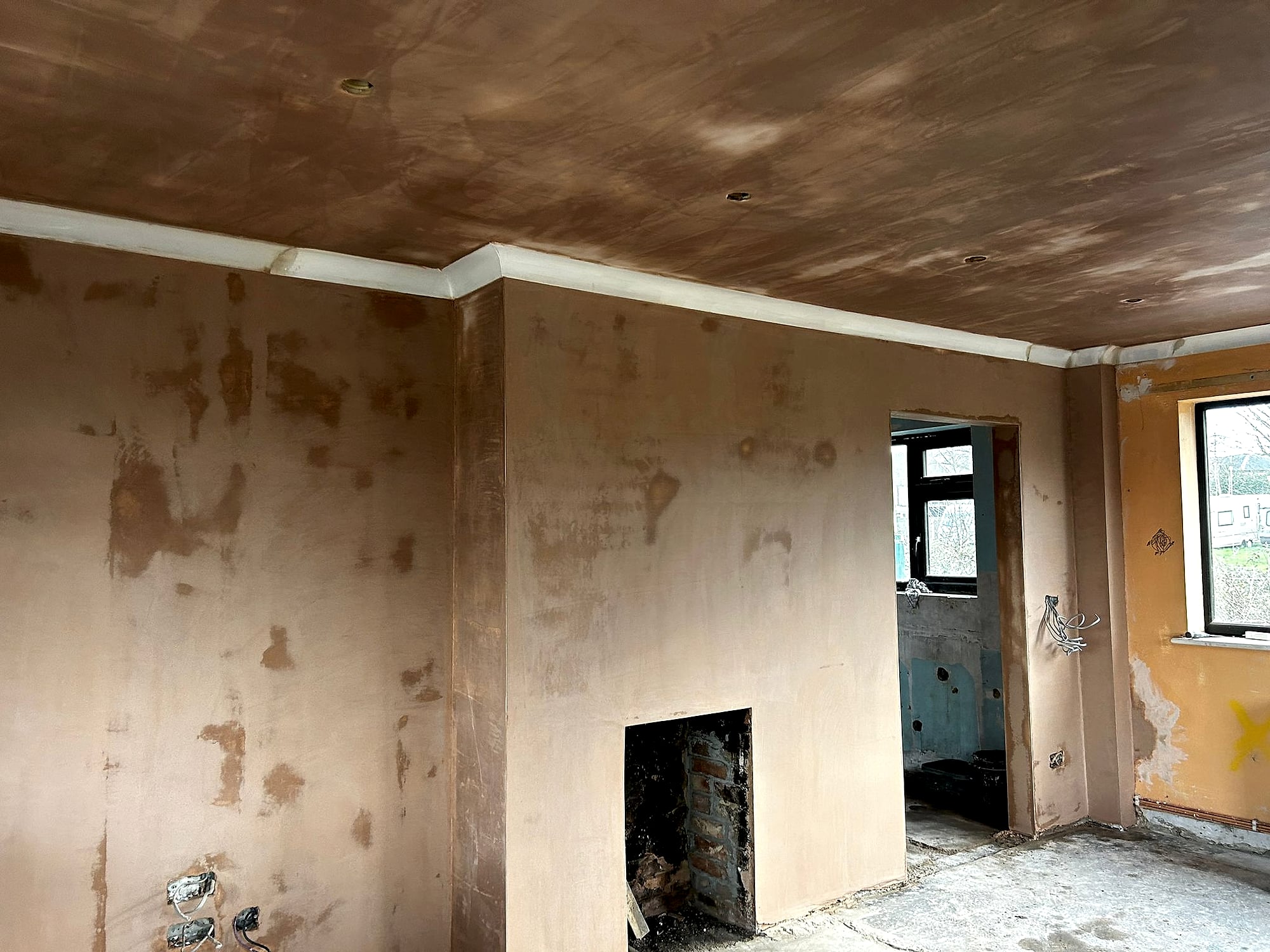 New build room with freshly skimmed walls and ceiling showing fireplace opening and kitchen doorway in Kent