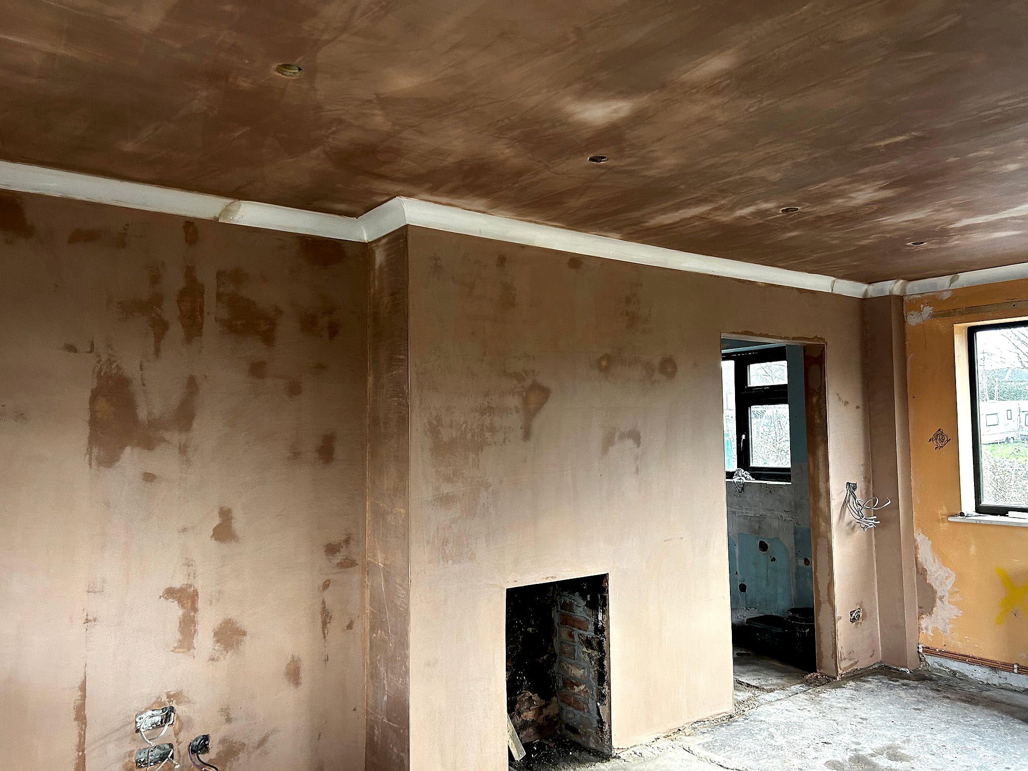 Freshly plastered walls and ceiling in new build room showing fireplace opening and black frame windows in Kent