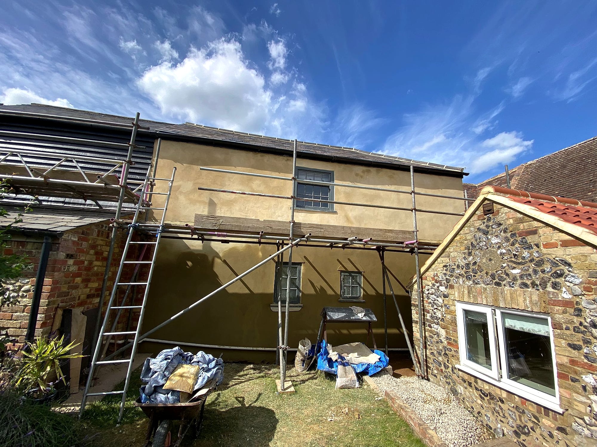 Sand and cement render on period cottage next to traditional Kent flint wall with scaffolding on sunny day