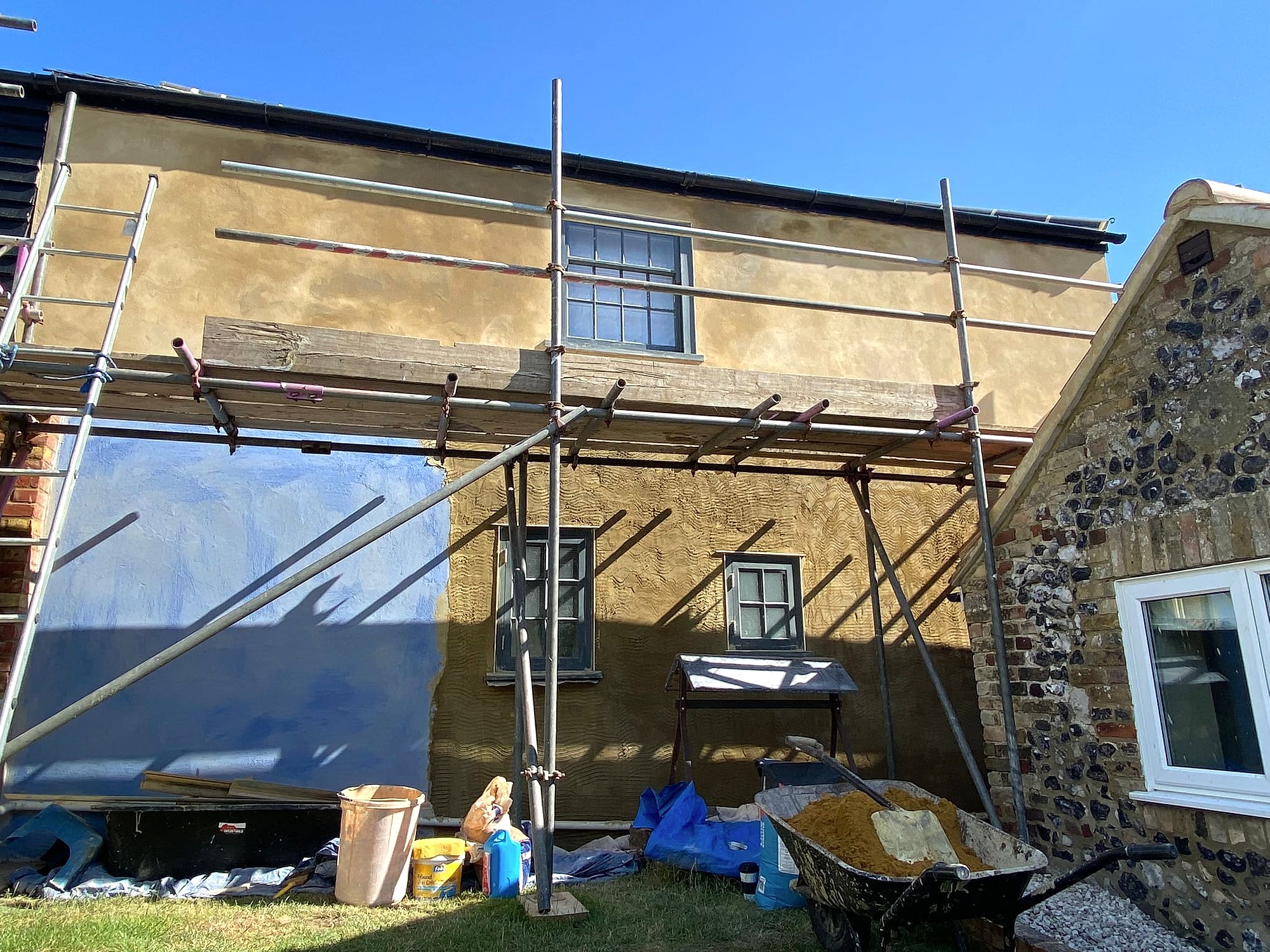 Completed sand and cement render on period cottage ground floor with scaffolding and flint outbuilding in Kent