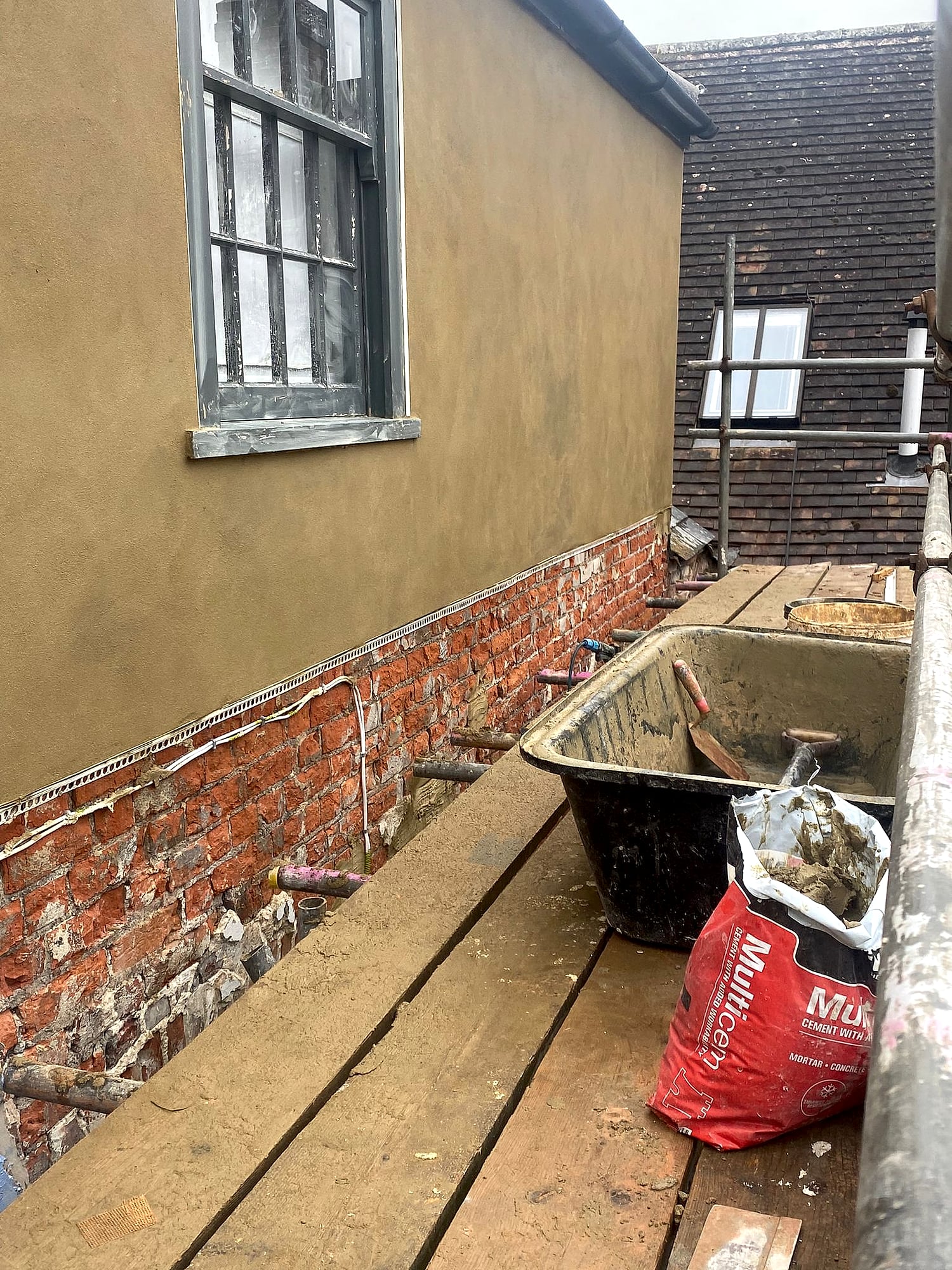 Fresh render applied up to eaves with cement trough on scaffolding boards during exterior rendering in Kent