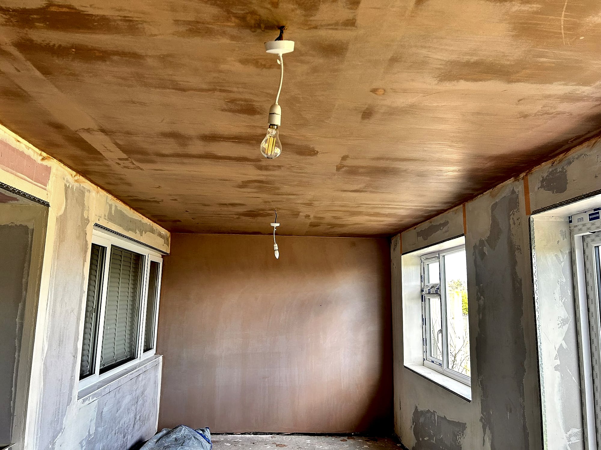 Room with freshly skimmed ceiling drying over plasterboard walls with multiple windows in Kent property