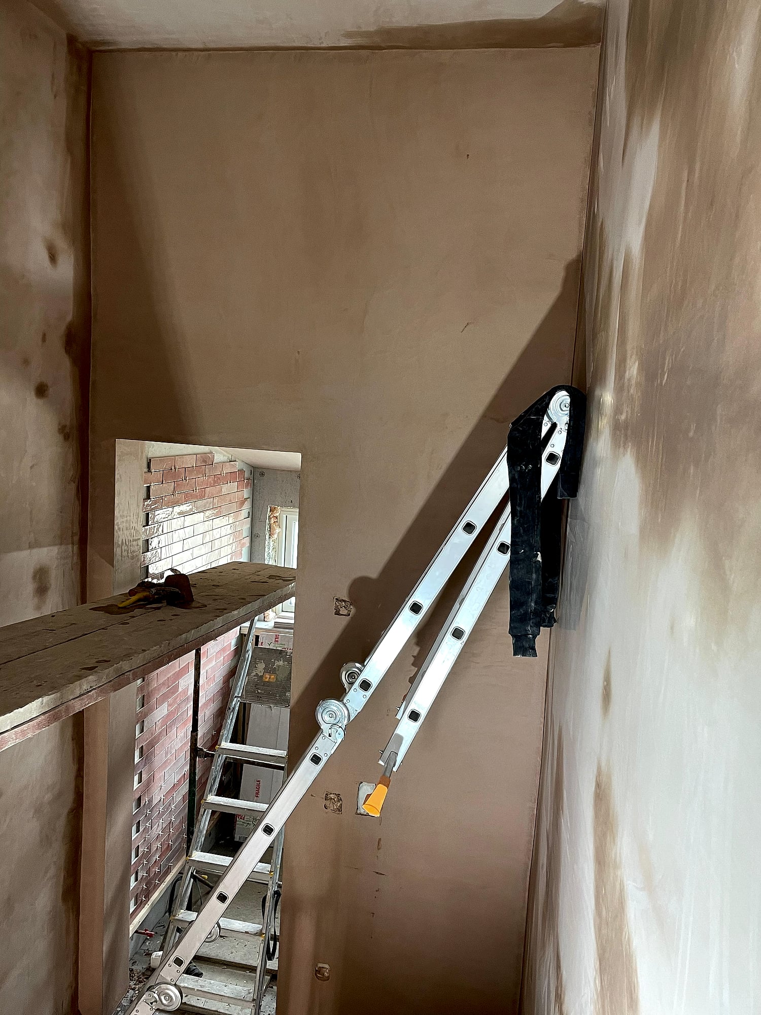 Tall stairwell walls freshly plastered with scaffold board and ladder access in Kent property