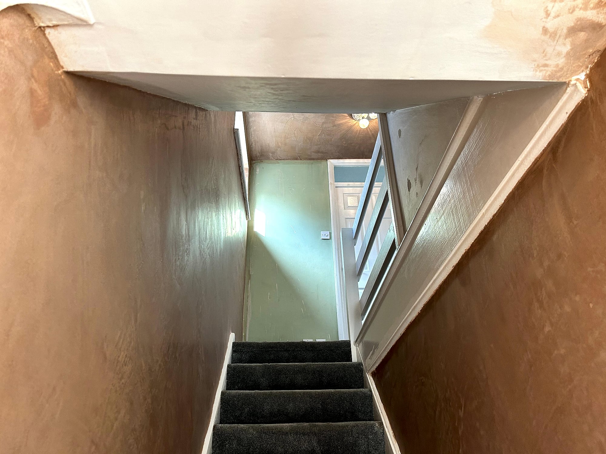 Freshly plastered stairwell walls looking down carpeted stairs with smooth plaster finish in Kent home