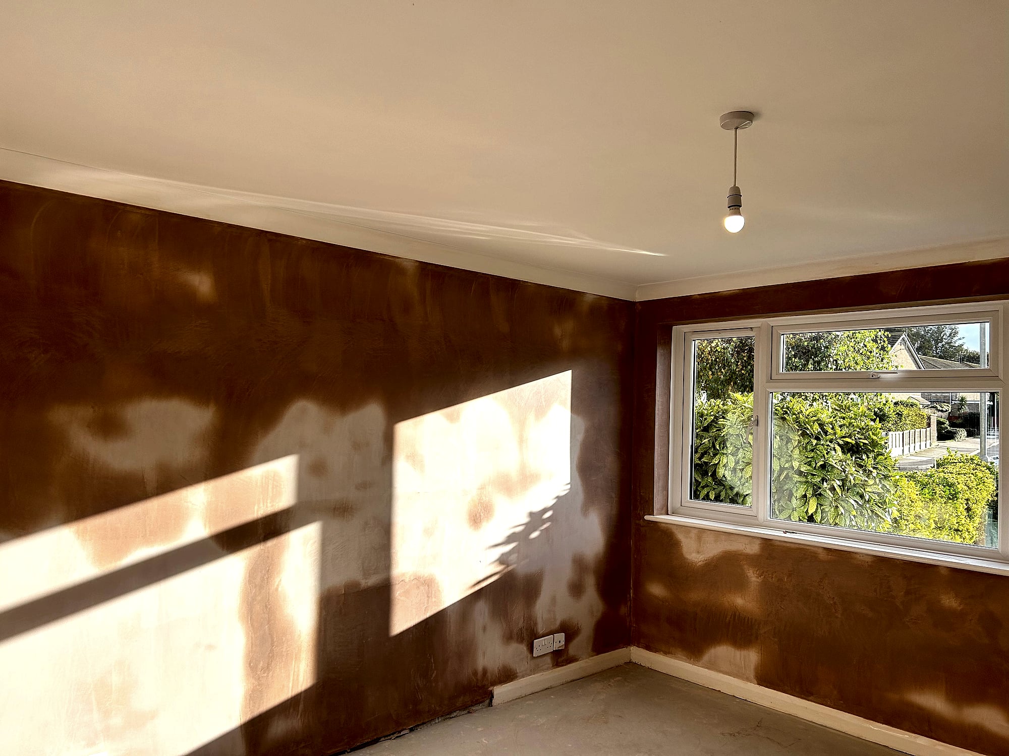 Freshly plastered bedroom walls with smooth skim coat finish and sunlight streaming through garden window in Kent