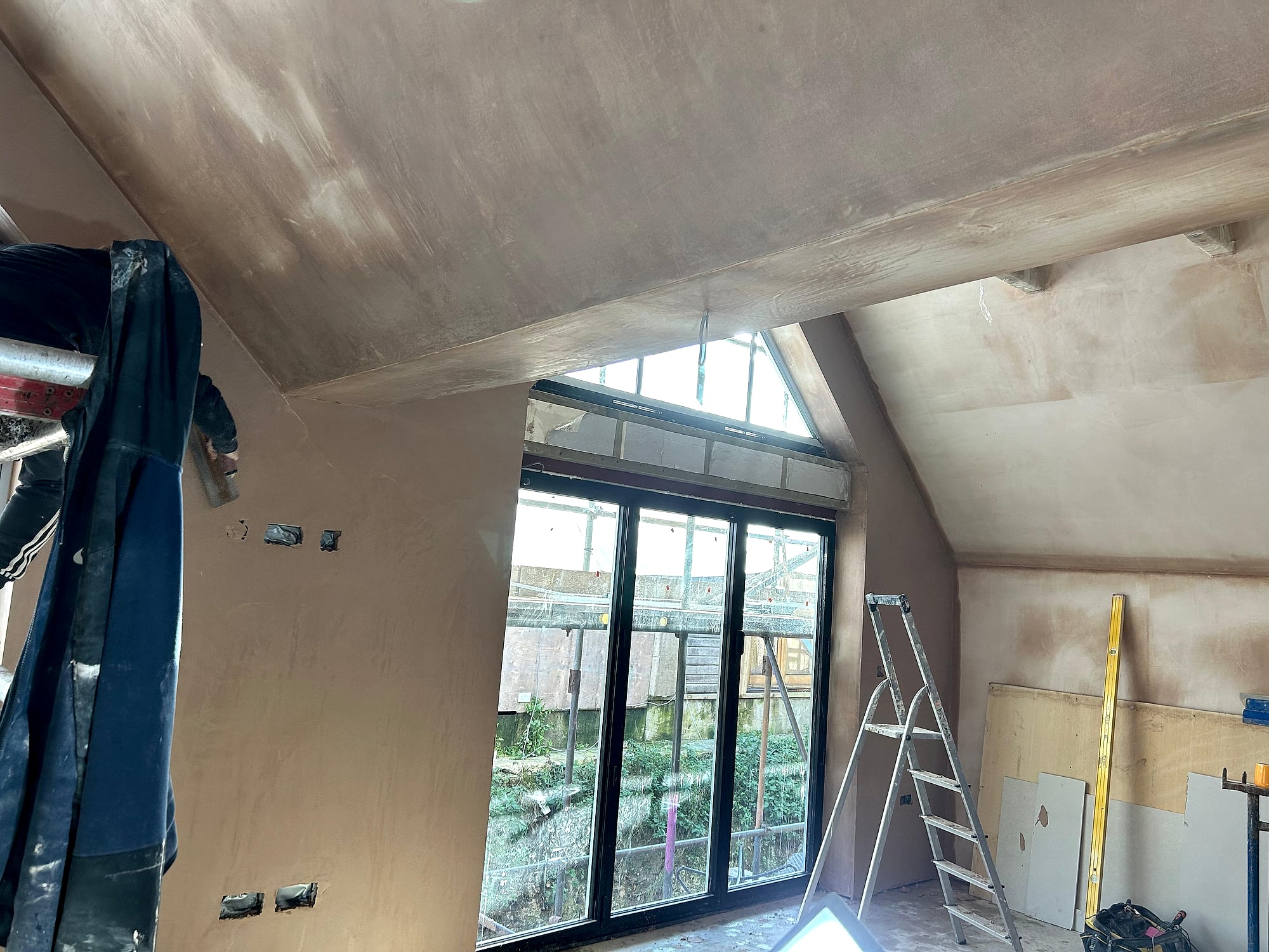 Fresh skim coat drying on vaulted ceiling with exposed beam and bifold garden doors in Kent extension