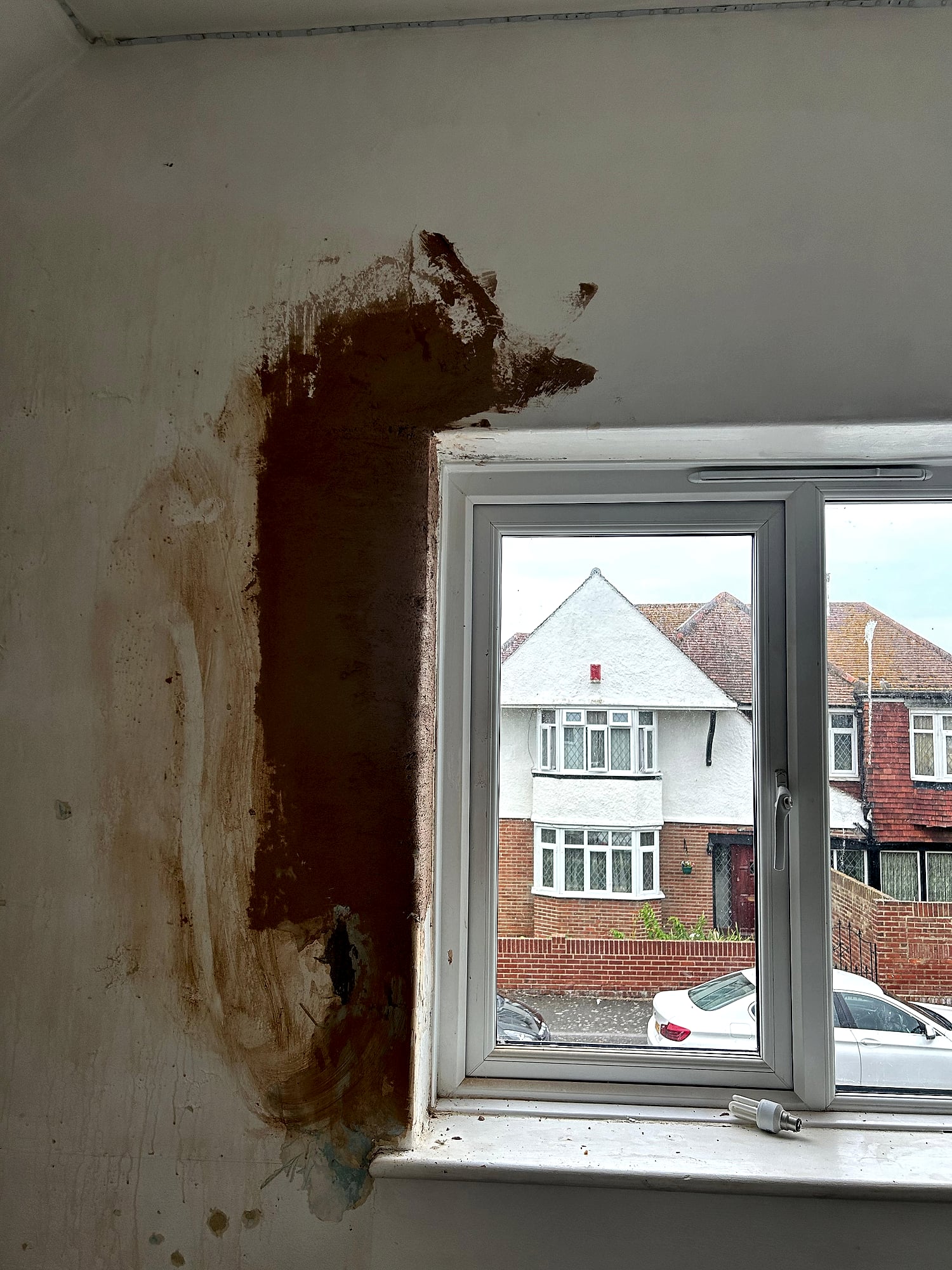 Window reveal being re-plastered showing wet brown coat next to wallpapered wall in Kent home